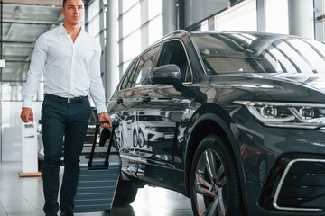 Partical view. Man in formal clothes is with luggage indoors near the car
