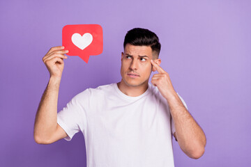 Photo of minded young thoughtful man look hold hand heart icon finger head isolated on violet color...