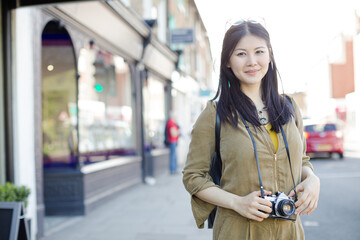 Fototapeta premium Portrait smiling, confident young female tourist with camera on sunny urban street
