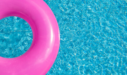 Summer banner with pink inflatable ring in blue swimming pool, surface with waves, textured water. Top view. Copy space