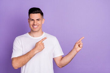 Photo of positive happy young man point fingers empty space information isolated on purple color background