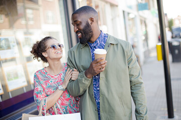 Affectionate young couple with coffee and shopping bag outside storefront
