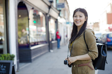 Portrait smiling, confident young female tourist with camera on sunny urban street