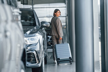 Fototapeta na wymiar Holding luggage. Woman is indoors near brand new automobile indoors