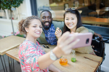 Smiling young friends taking selfie with camera phone at sidewalk cafe