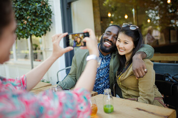 Obraz premium Woman photographing affectionate couple friends with camera phone at sidewalk cafe