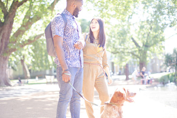 Happy young couple walking dog in sunny park