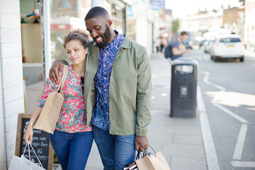 Affectionate young couple with shopping bag walking along storefront