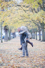 Fototapeta premium Senior man carrying woman on his back in autumn park