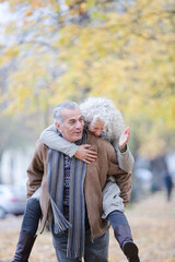 Fototapeta premium Senior man carrying woman on his back in autumn park