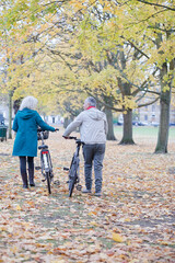 Senior couple walking bicycles among trees and leaves in autumn park