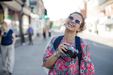 Fototapeta na wymiar Portrait laughing, enthusiastic young female tourist in sunglasses photographing with camera on urban street