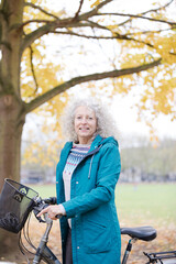 Fototapeta na wymiar Senior woman holding bike among autumn leaves in park