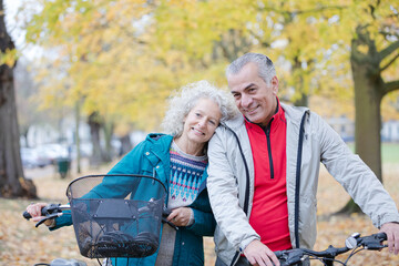 Senior couple walking bicycles among trees and leaves in autumn park