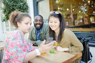Obraz premium Young friends using smart phone at sidewalk cafe