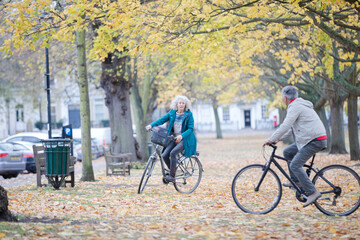 Fototapeta premium Senior couple bike riding among trees and leaves in autumn park