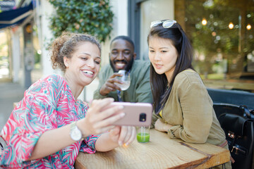 Smiling young friends taking selfie with camera phone at sidewalk cafe