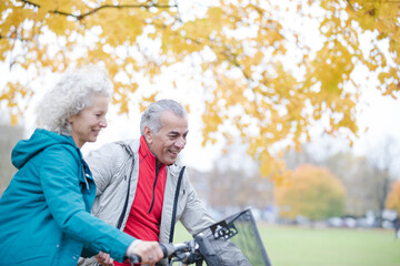 Senior couple bike riding among trees and leaves in autumn park