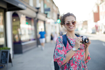 Fototapeta na wymiar Portrait laughing, enthusiastic young female tourist in sunglasses photographing with camera on urban street