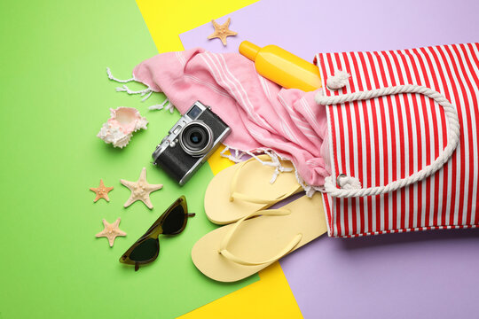 Stylish bag with beach accessories on color background, flat lay