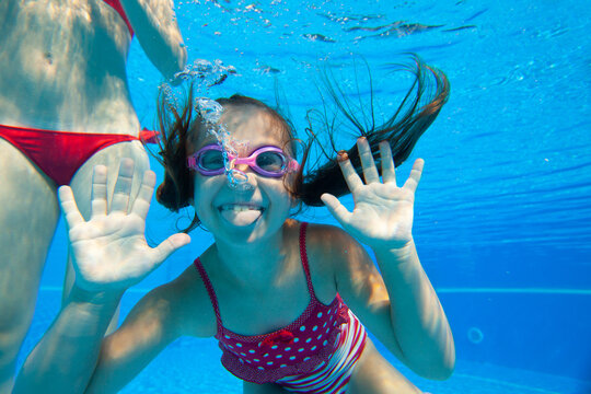 Cheerful little girl swiming under  water in pool.