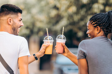 Two young people of different ethnicities toasting with a shake outdoors