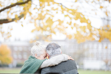 Carefree, affectionate senior couple hugging on bench in autumn park