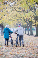 Senior couple walking bicycles among trees and leaves in autumn park