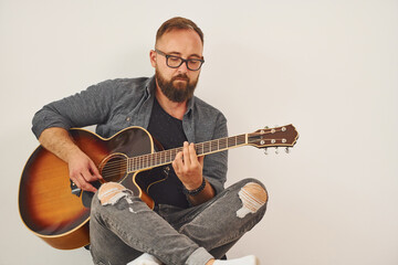 In the studio. Man in casual clothes and with acoustic guitar is indoors