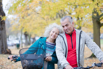 Senior couple walking bicycles among trees and leaves in autumn park