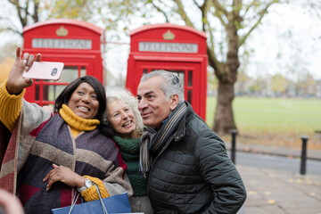 Fototapeta na wymiar Senior friends taking selfie in front of red telephone booths in autumn park