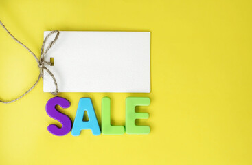 On a yellow background, there is a tag for the price tag and the word sale made of colored plastic letters. The concept of discounts and sales. Space for text