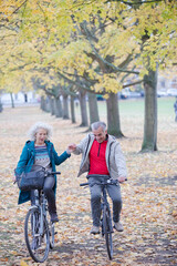 Senior couple bike riding among trees and leaves in autumn park