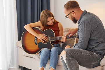 Private lesson. Guitar teacher showing how to play the instrument to young woman
