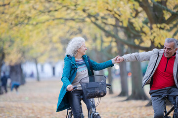 Obraz premium Senior couple bike riding among trees and leaves in autumn park