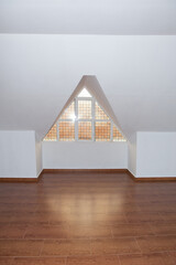 Loft, ático vacío con suelo de madera, paredes blancas y ventana triangular de vidrio. Lugar...