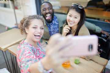 Smiling young friends taking selfie with camera phone at sidewalk cafe