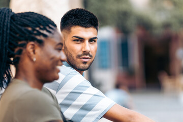 Young caucasian man facing the camera next to an afro woman outdoors