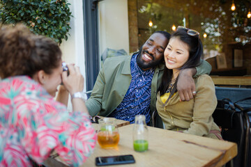 Obraz premium Woman photographing affectionate couple friends with camera phone at sidewalk cafe