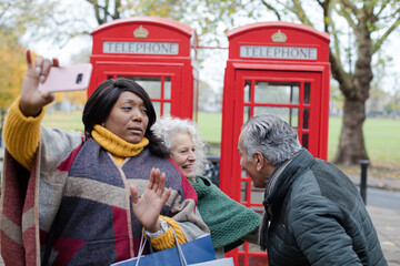 Obraz premium Senior friends taking selfie in front of red telephone booths in autumn park