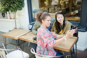 Smiling young friends taking selfie with camera phone at sidewalk cafe