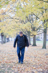 Fototapeta premium Senior man walking among leaves in autumn park