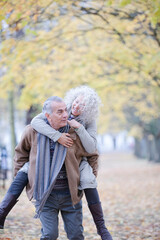 Senior man carrying woman on his back in autumn park