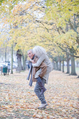 Senior man carrying woman on his back in autumn park