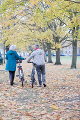 Senior couple walking bicycles among trees and leaves in autumn park