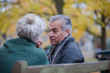 Happy senior couple sharing headphones, listening to music in park