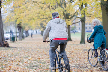 Senior couple bike riding among leaves and trees in autumn park