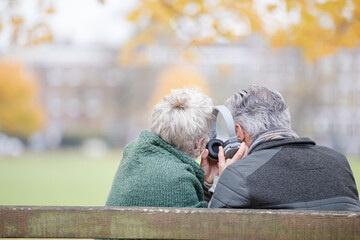 Happy senior couple sharing headphones, listening to music in park