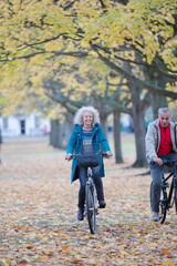 Senior couple bike riding among trees and leaves in autumn park