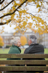 Affectionate senior couple talking on bench in autumn park